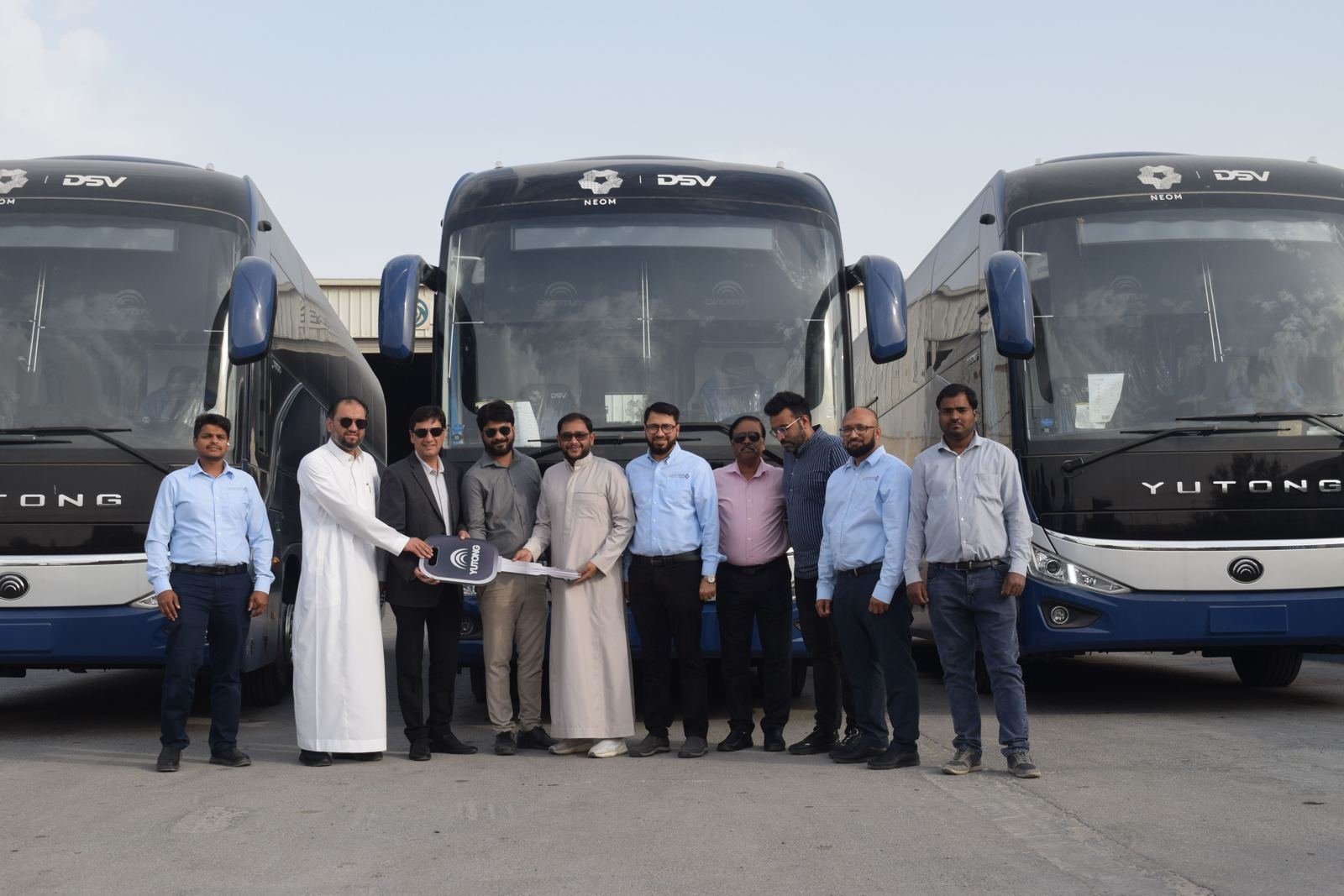 Business team handing over vehicle keys in front of coaches